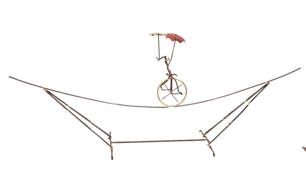 Freestanding metal sculpture depicting an acrobatic unicyclist, balancing with two umbrellas, one brass and one copper, with the unicycle supported on an intricate metal tightrope structure.