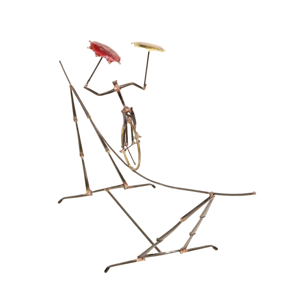 Freestanding metal sculpture depicting an acrobatic unicyclist, balancing with two umbrellas, one brass and one copper, with the unicycle supported on an intricate metal tightrope structure.