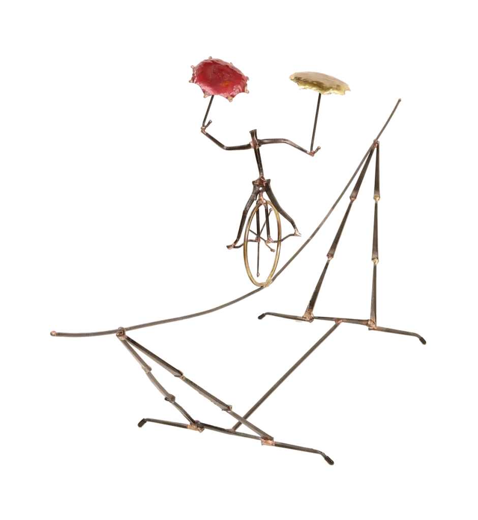 Freestanding metal sculpture depicting an acrobatic unicyclist, balancing with two umbrellas, one brass and one copper, with the unicycle supported on an intricate metal tightrope structure.
