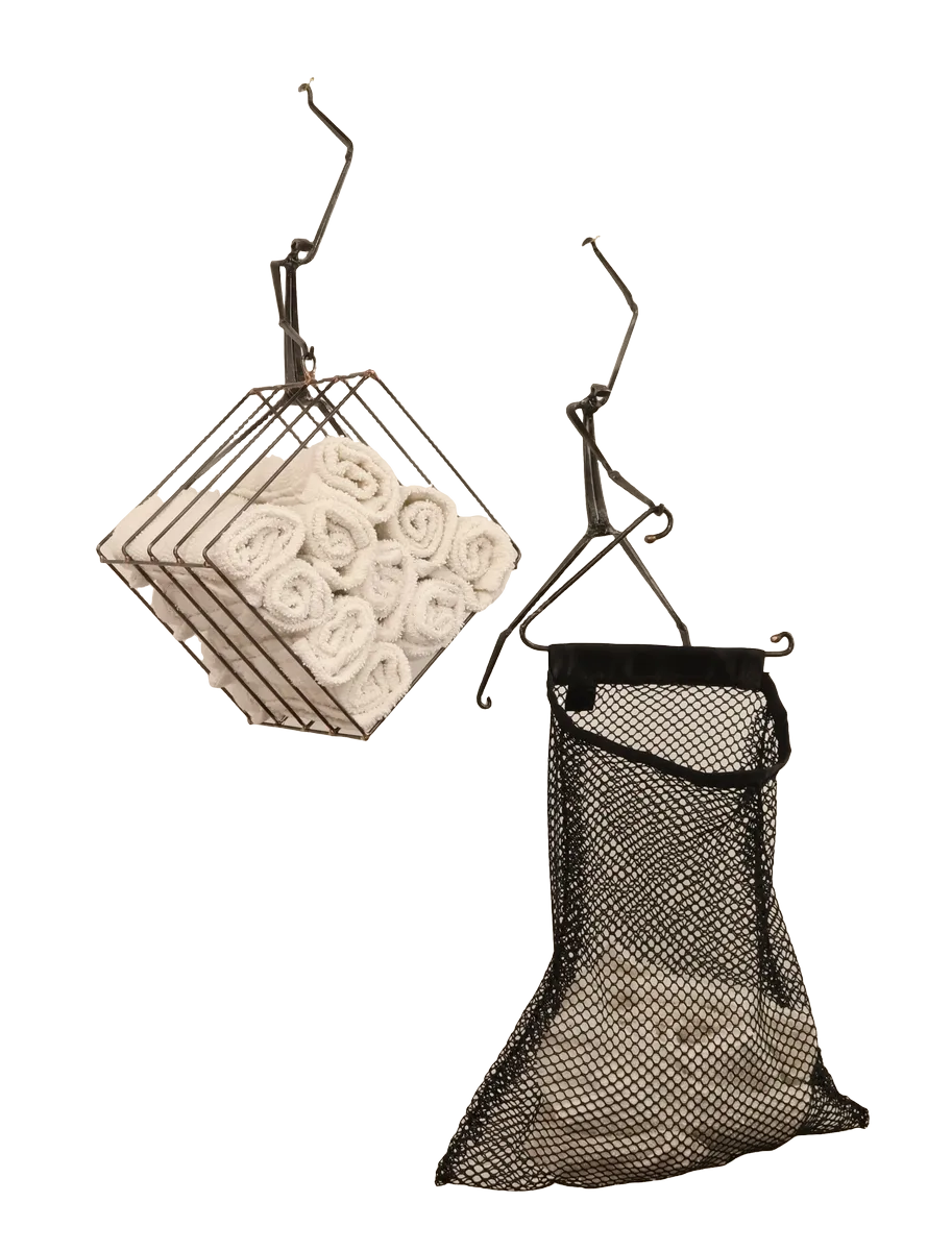 Wall-mounted bathroom storage unit metal sculpture with rolled white towels in a steel wire basket, a black polyester mesh removable laundry bag for soiled hand towels hanging below from a steel hanger and incorporating a dock side theme with a decorative steel dragonfly, copper and brass reed accents and steel birds in flight from a brass dock pier.