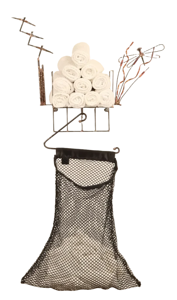 Wall-mounted bathroom storage unit metal sculpture with rolled white towels in a steel wire basket, a black polyester mesh removable laundry bag for soiled hand towels hanging below from a steel hanger and incorporating a dock side theme with a decorative steel dragonfly, copper and brass reed accents and steel birds in flight from a brass dock pier.