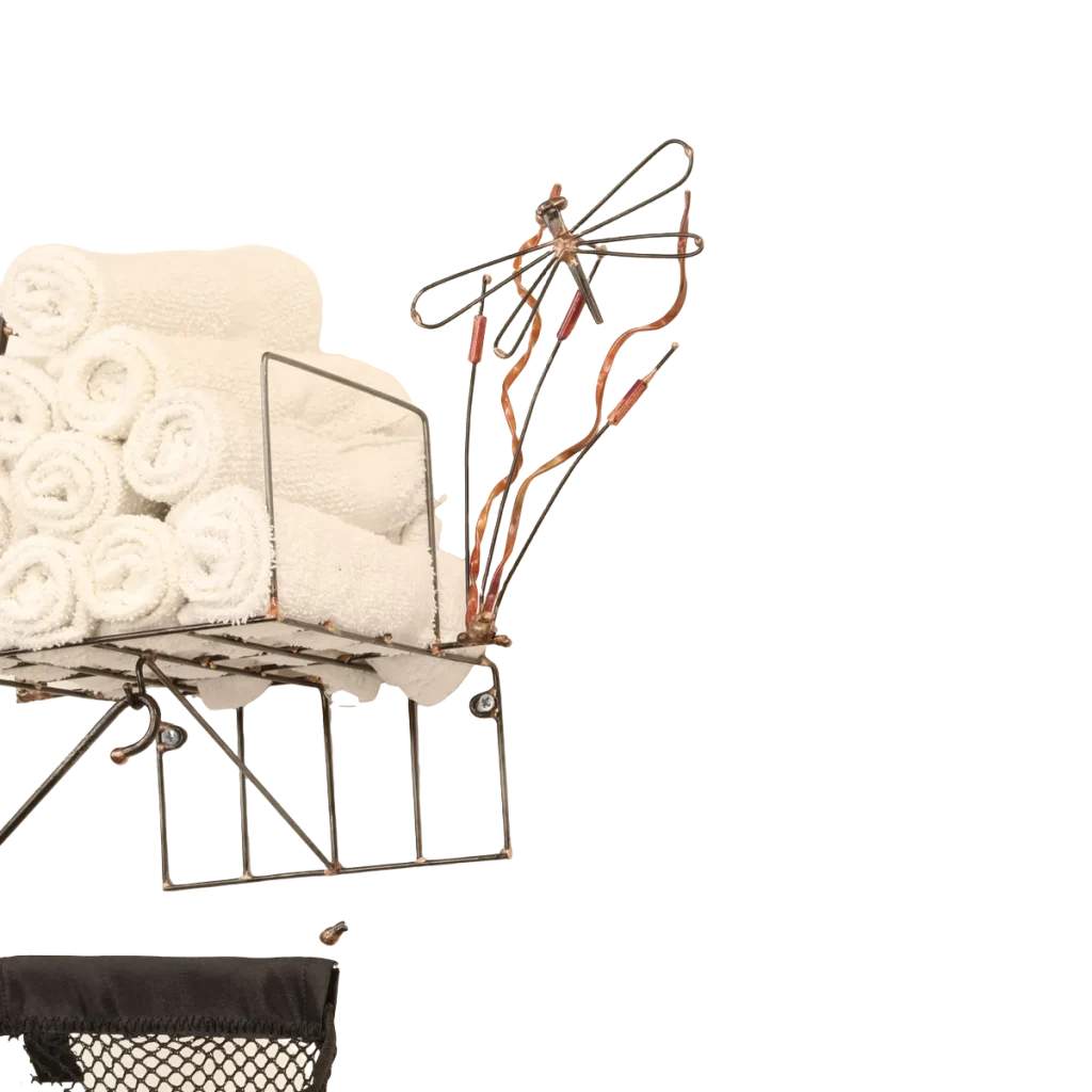 Wall-mounted bathroom storage unit metal sculpture with rolled white towels in a steel wire basket, a black polyester mesh removable laundry bag for soiled hand towels hanging below from a steel hanger and incorporating a dock side theme with a decorative steel dragonfly, copper and brass reed accents and steel birds in flight from a brass dock pier.