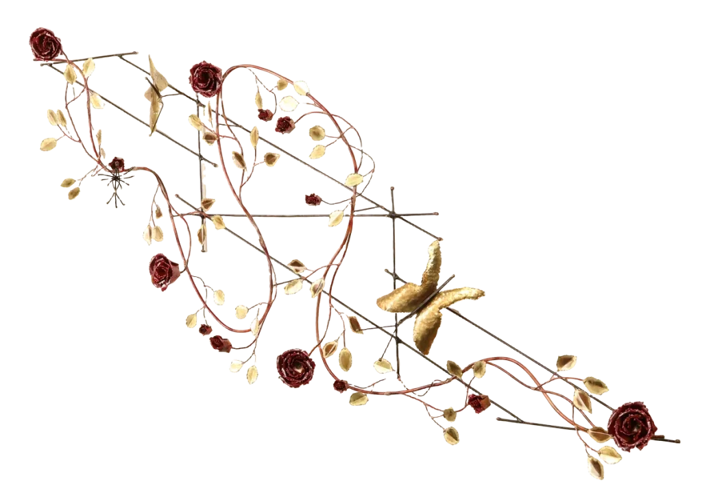 Decorative metal wall art depicting a trellis-like structure adorned with brass leaves, deep red copper roses of three different sizes, a brass butterfly and steel wire hummingbird feeding from one of the copper roses. A small spider-like figure is visible near the upper left.