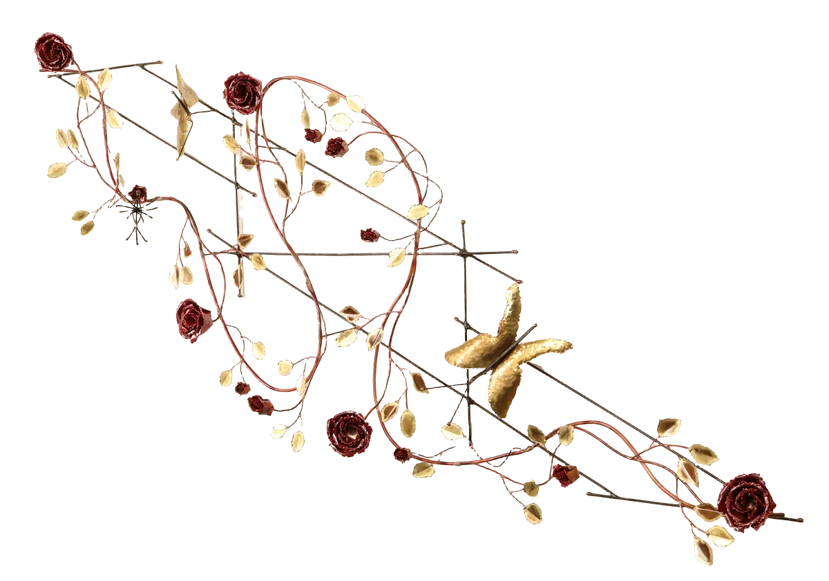 Decorative metal wall art depicting a trellis-like structure adorned with brass leaves, deep red copper roses of three different sizes, a brass butterfly and steel wire hummingbird feeding from one of the copper roses. A small spider-like figure is visible near the upper left.