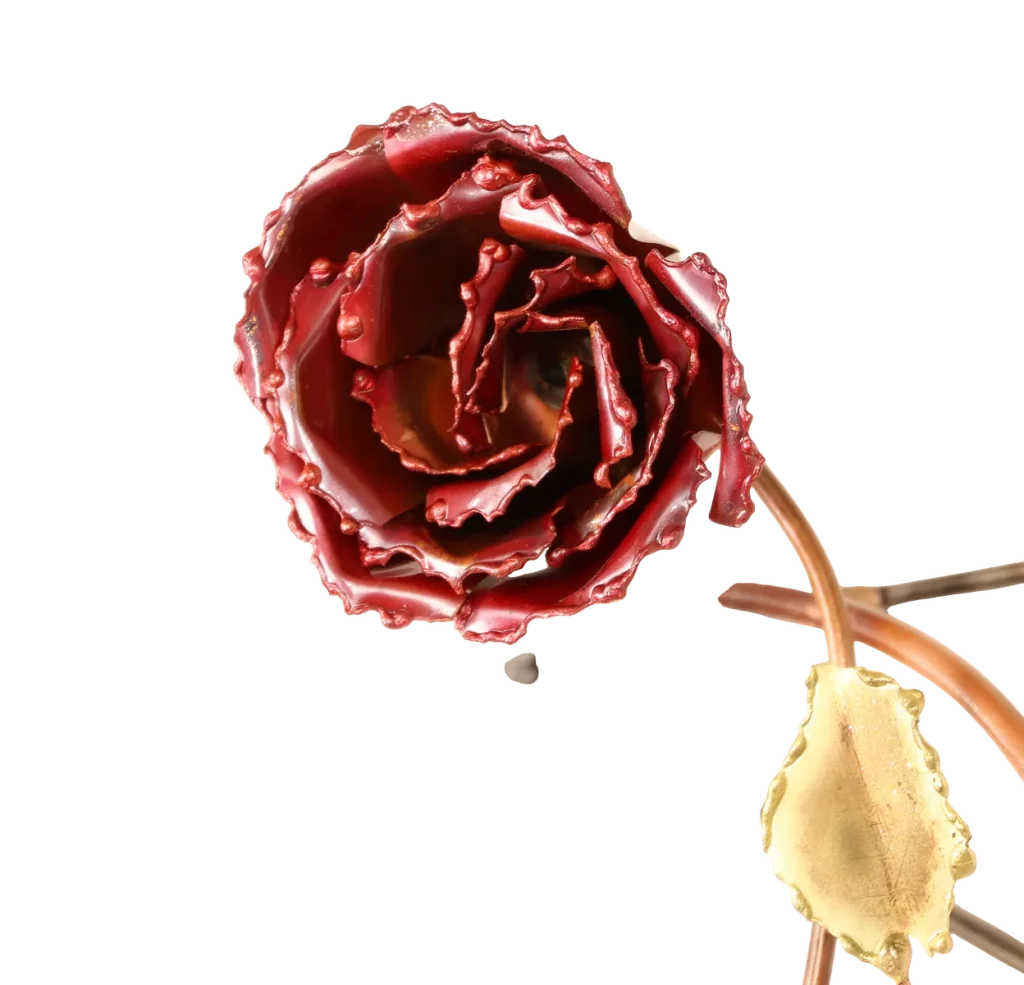 Decorative metal wall art depicting a trellis-like structure adorned with brass leaves, deep red copper roses of three different sizes, a brass butterfly and steel wire hummingbird feeding from one of the copper roses. A small spider-like figure is visible near the upper left.