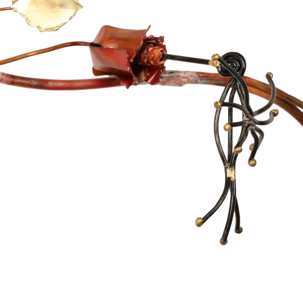 Decorative metal wall art depicting a trellis-like structure adorned with brass leaves, deep red copper roses of three different sizes, a brass butterfly and steel wire hummingbird feeding from one of the copper roses. A small spider-like figure is visible near the upper left.