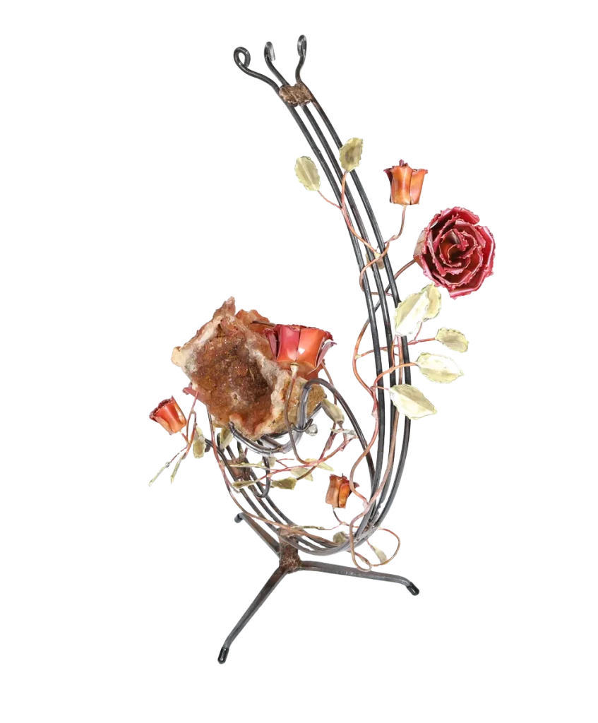 A handcrafted metal sculpture featuring a large open quartz geode nestled in the center. The open geode is supported in a semi-circular steel structure. Several copper roses and brass leaves embellish the structure, which has a metal base for stability.