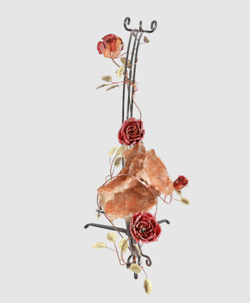 A handcrafted metal sculpture featuring a large open quartz geode nestled in the center. The open geode is supported in a semi-circular steel structure. Several copper roses and brass leaves embellish the structure, which has a metal base for stability.
