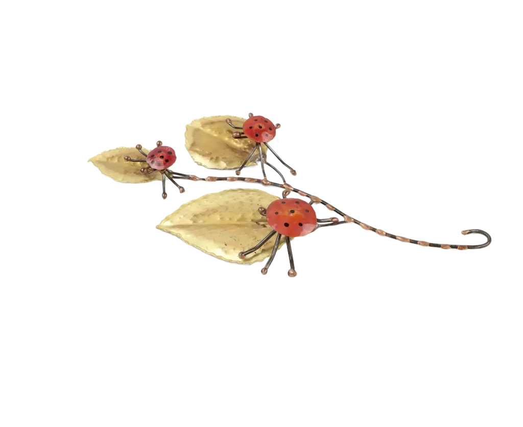 Freestanding metal sculpture showing three copper and steel ladybugs poised on the large brass leaves of a leafy branch