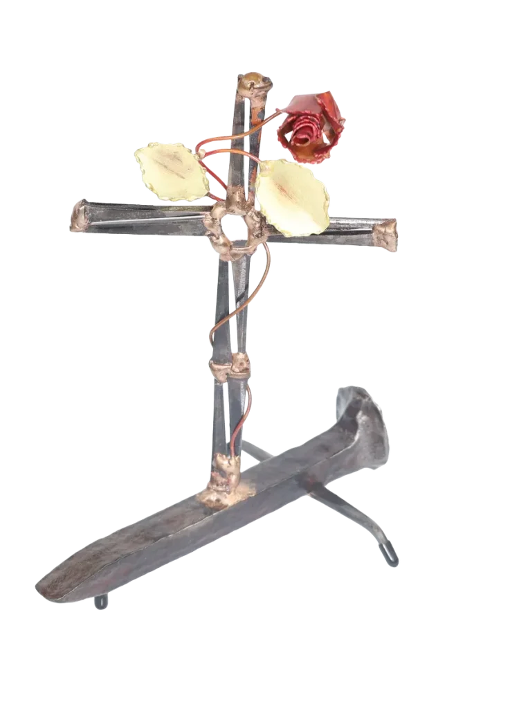 Handcrafted metal cross made of steel cut nails and mounted on a railroad spike, with a decorative copper rose, copper vine and brass leaves twisted around the cross from its base.