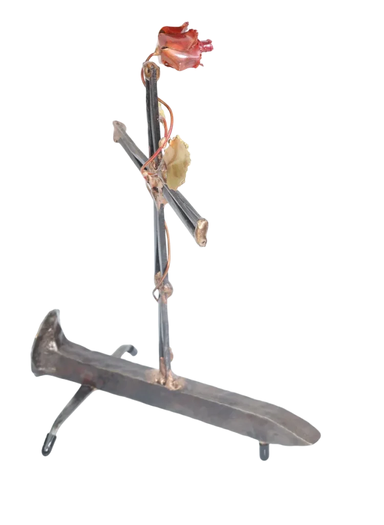 Handcrafted metal cross made of steel cut nails and mounted on a railroad spike, with a decorative copper rose, copper vine and brass leaves twisted around the cross from its base.