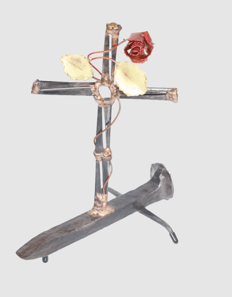 Handcrafted metal cross made of steel cut nails and mounted on a railroad spike, with a decorative copper rose, copper vine and brass leaves twisted around the cross from its base.