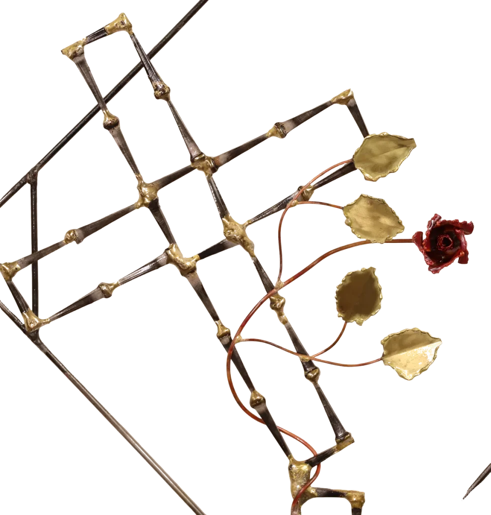 Handmade metal wall art depicting a broken cross made of steel cut nails with a copper rose and vine with brass leaves, growing out of the break in the cross. The broken cross is framed in a steel diamond shape with decorative curls. The broken cross and rose are symbolic of the resurrection of Jesus after crucifixion.