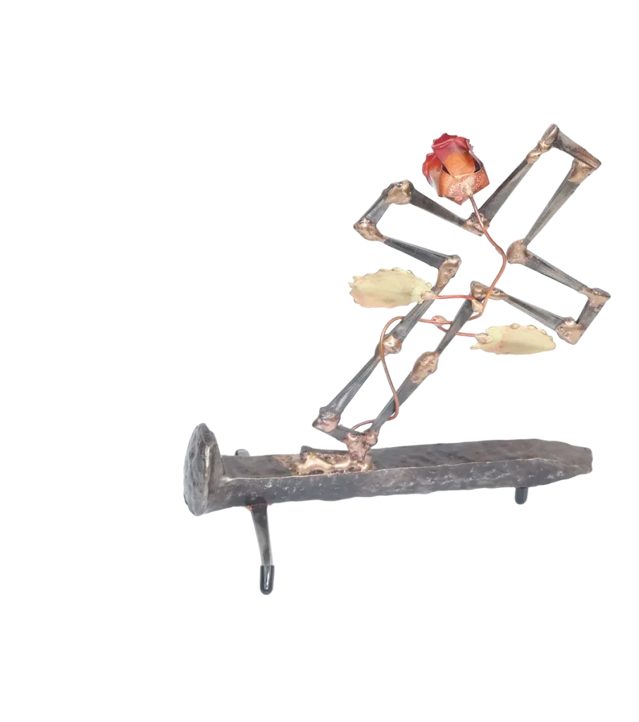 Freestanding metal sculpture depicting a broken cross made of cut steel nails and mounted on a railroad spike with a copper rose and vine with brass leaves, growing out of the break in the cross. The broken cross and rose is symbolic of the resurrection of Jesus after crucifixion.