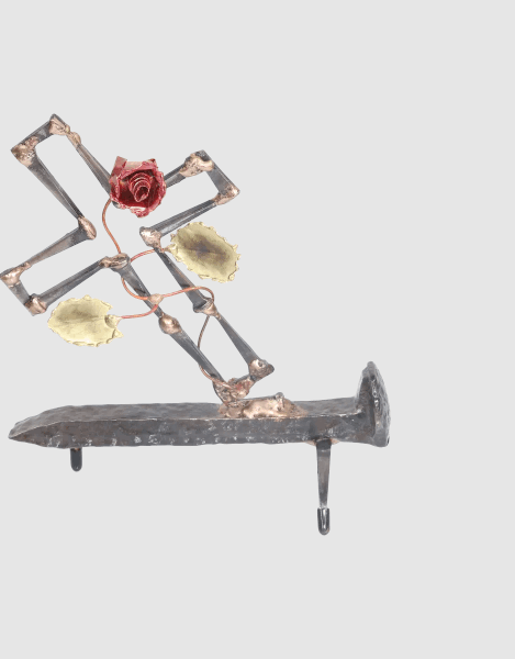 Freestanding metal sculpture depicting a broken cross made of cut steel nails and mounted on a railroad spike with a copper rose and vine with brass leaves, growing out of the break in the cross. The broken cross and rose is symbolic of the resurrection of Jesus after crucifixion.