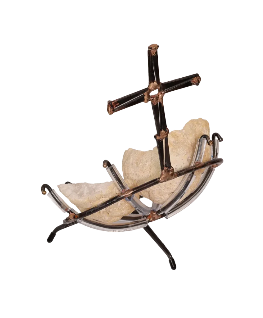 A handmade metal sculpture featuring a cross made of steel cut nails and rising above two white geode halves held within a steel clear vinyl padded frame resting on a tripod base.